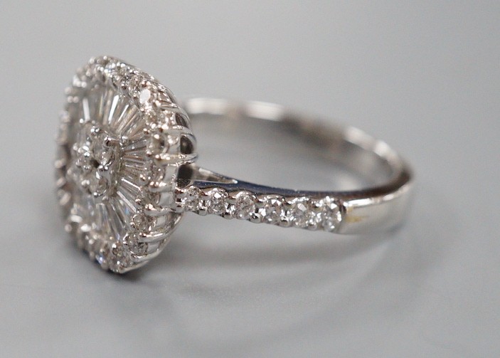 A modern 750 white metal, trapeze and round cut diamond set cushion shaped cluster dress ring, with diamond set shoulders, size M, gross weight 5.7 grams